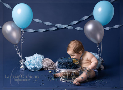Baby boy faceplanting eating birthday cake navy cake smash with balloons cambridge peterborough huntingdon cake smash photos little cherubs photography studio