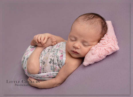 Little new baby girl curled up on purple blanket with floral wrap and pink pillow chatteris ely cambridge newborn photography studio little cherubs