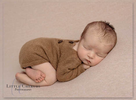 Newborn baby boy in brown button romper laying on his front march peterborough new baby photographer little cherubs studio
