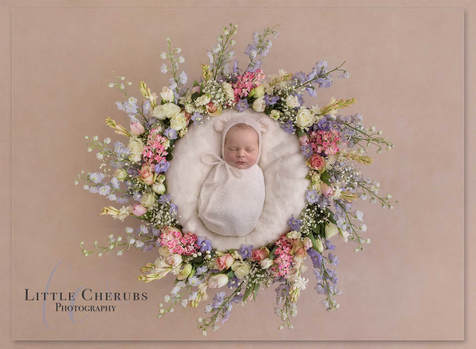 newborn baby wrapped in white with bear ears in a pastel flower wreath little cherubs photography studio peterborough